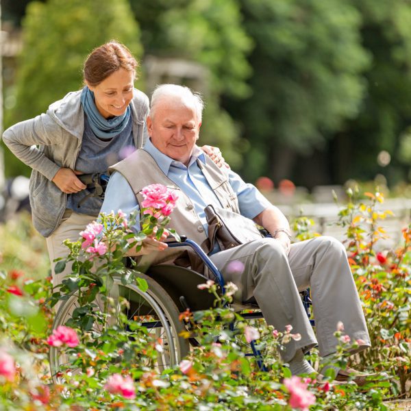 Caregiver and senior man on a wheelchair walking outdoors